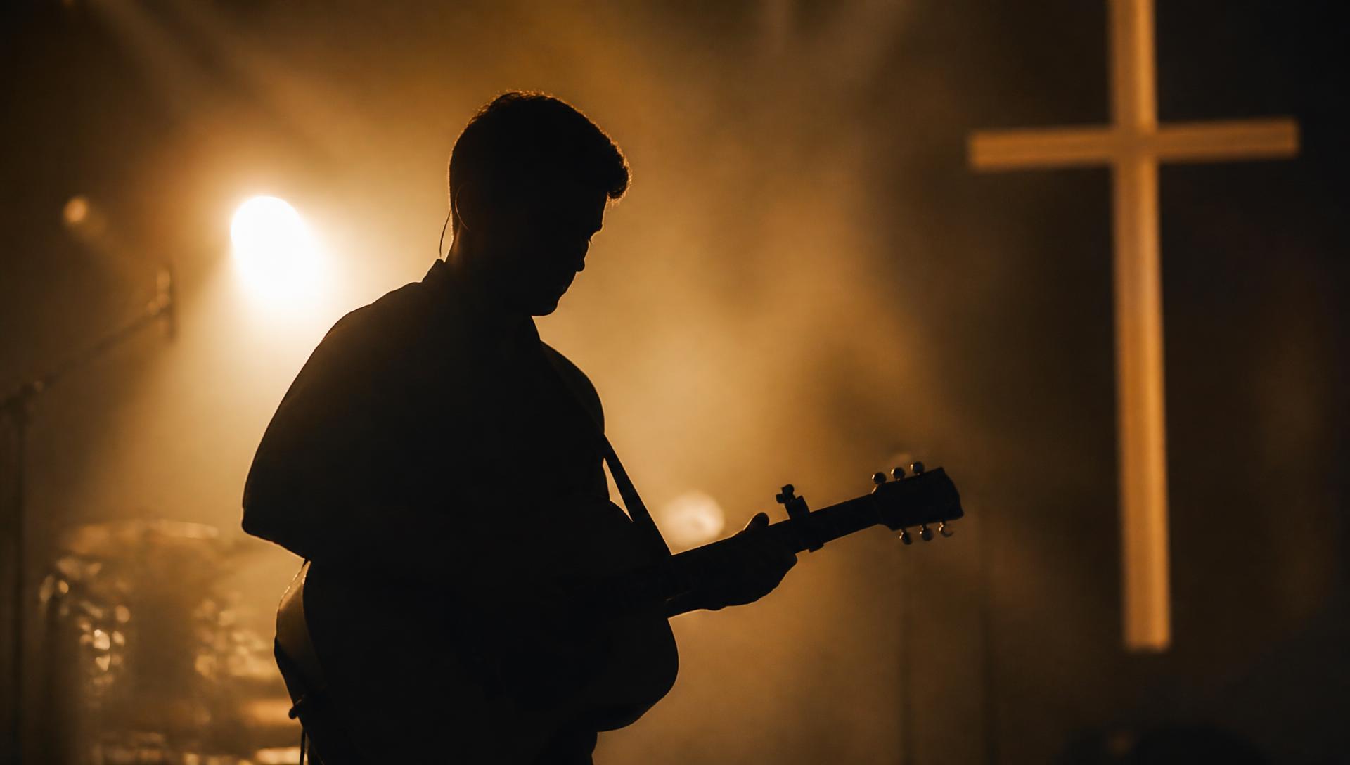 Isac Gomes tocando violão em um palco iluminado